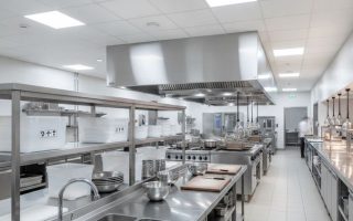 Layout de cozinha profissional com bancadas, pias, estantes e coifa industrial em aço inox