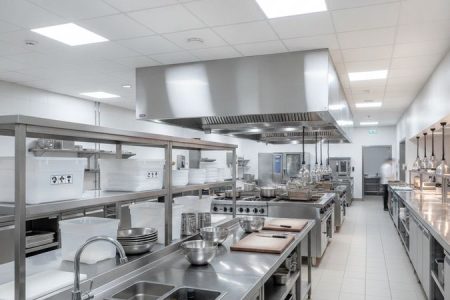 Layout de cozinha profissional com bancadas, pias, estantes e coifa industrial em aço inox