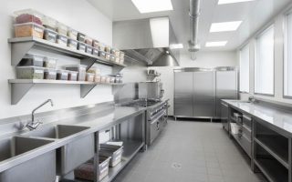 Cozinha profissional organizada com bancadas, prateleiras, pia industrial e armários de aço inox