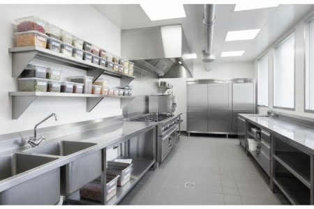 Cozinha profissional organizada com bancadas, prateleiras, pia industrial e armários de aço inox