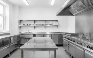 Cozinha industrial equipada com bancada, pia, prateleiras e coifa em aço inox para manipulação de alimentos